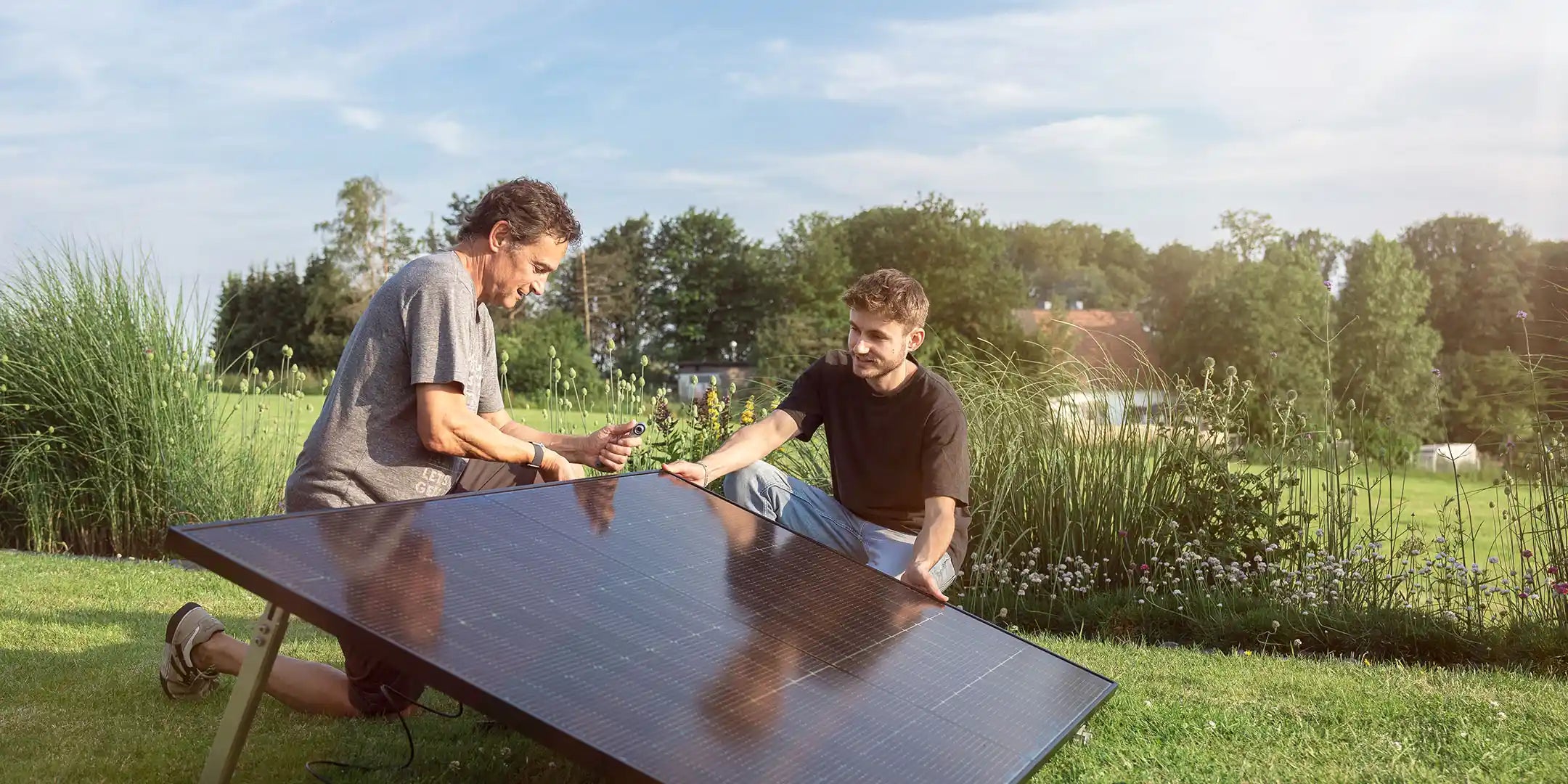 Zwei Männer schließen Balkonkraftwerk-Solarmodul im Garten an – Solago Shop Hero-Bild