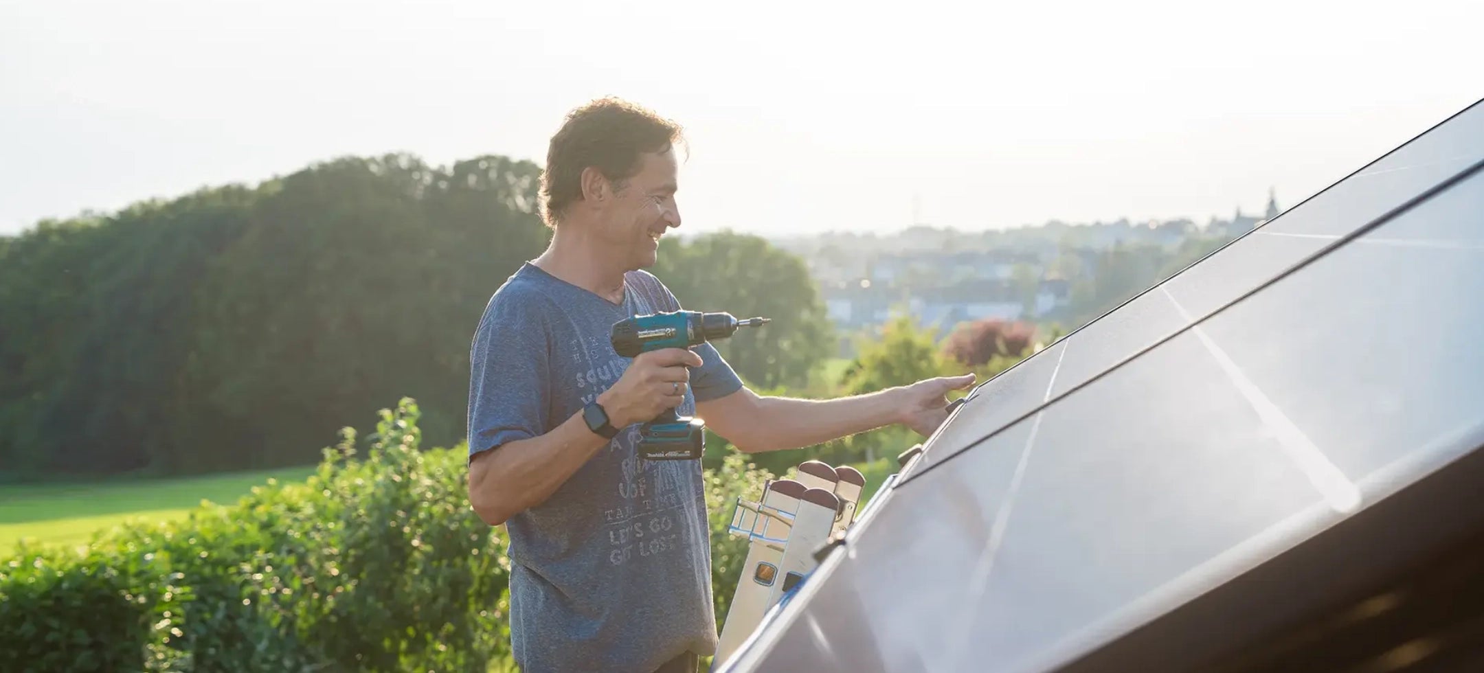 Mann montiert Balkonkraftwerk 800W Komplettset auf Schrägdach mit Bohrmaschine bei Sonnenschein