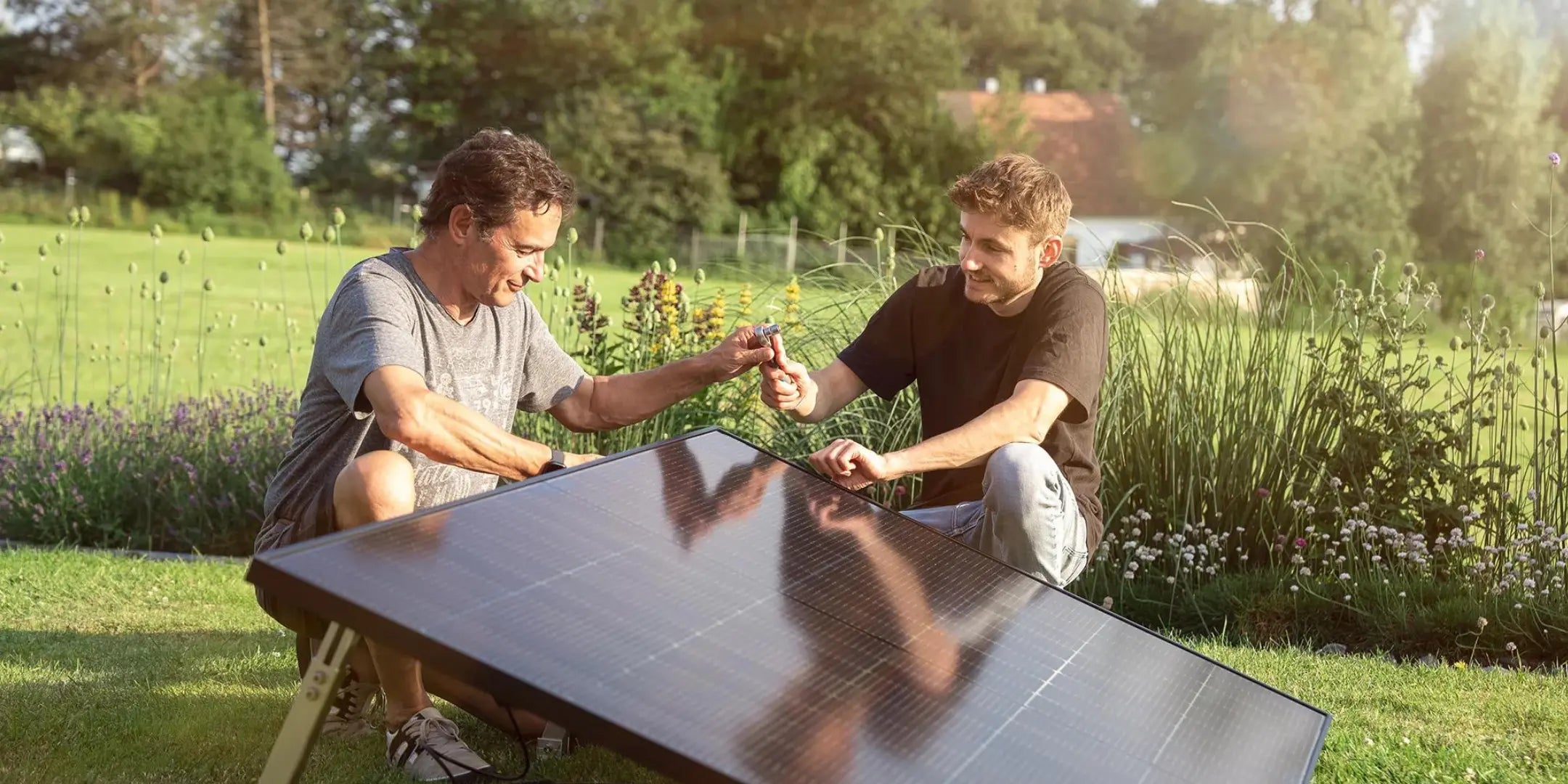 Zwei Männer stellen ein Balkonkraftwerk mit Solarmodul im Garten auf.