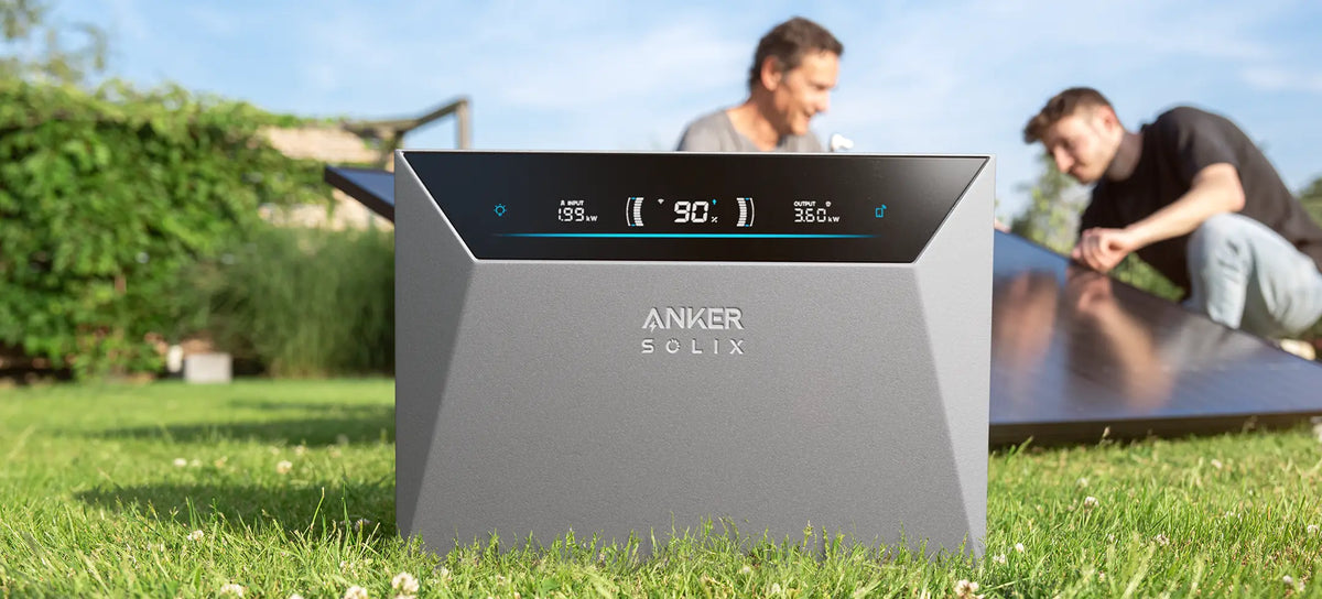 Anker SOLIX Solarbank Speicher für ein Balkonkraftwerk im Garten mit Solarmodulen im Hintergrund.