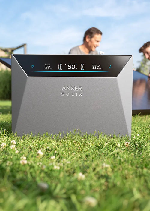 Anker SOLIX Solarbank Speicher für ein Balkonkraftwerk im Garten mit Solarmodulen im Hintergrund.