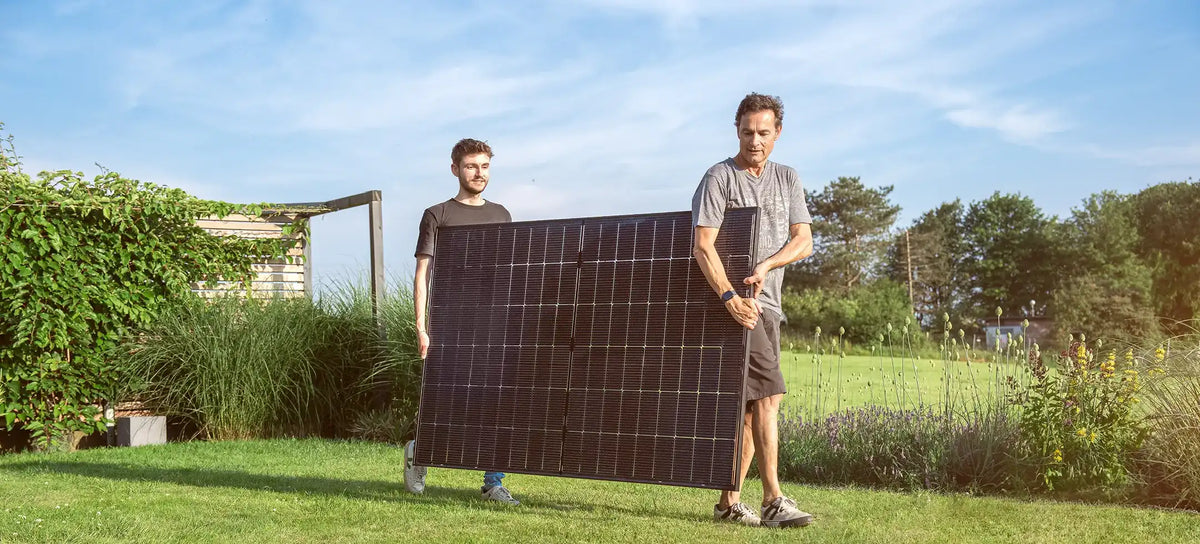 Zwei Männer tragen ein Solarmodul im Garten.