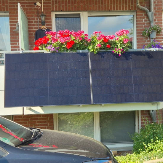 AIKO Balkonkraftwerk-Solarmodule an Balkongeländer eines Mehrfamilienhauses mit Blumenkästen