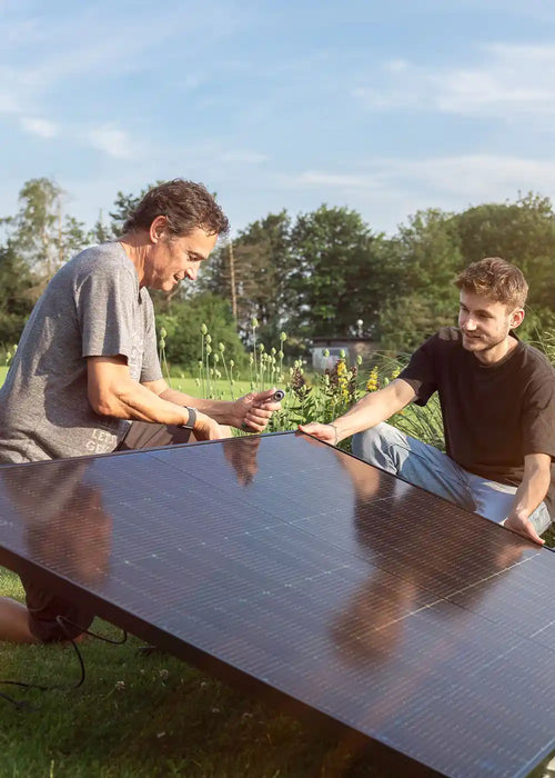 Zwei Männer schließen Balkonkraftwerk-Solarmodul im Garten an – Solago Shop Hero-Bild